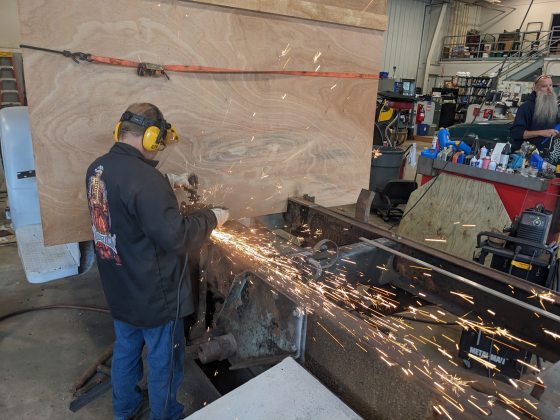 A person in a metal shop working on a truck frame.